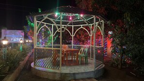 A gazebo with a table and chairs, surrounded by plants and colorful lights. - Cozy 1-bedroom farmhouse in serene Badlapur with AC (Badlapur)