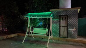 A swing set with a green canopy, a small building with a 'ROOM' sign, and a water fountain. - Cozy 1-bedroom farmhouse in serene Badlapur with AC (Badlapur)