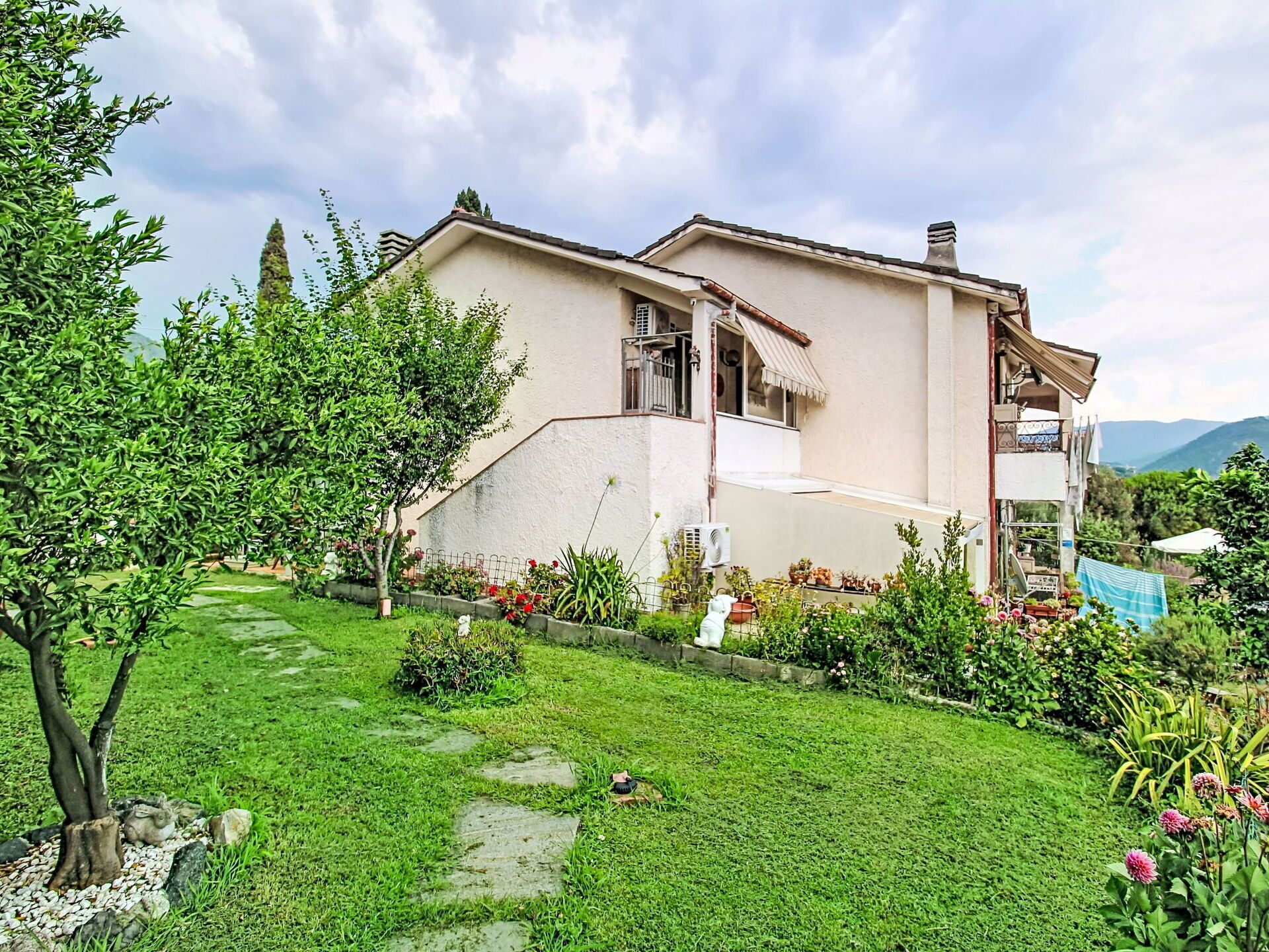 Une maison à deux étages avec un jardin, un chemin pavé et une vue sur les montagnes.
