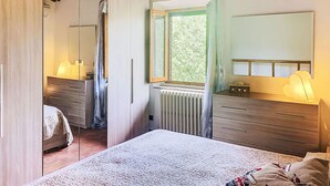 Un dormitorio con cama, cómoda, espejo, ventana con cortinas y radiador.