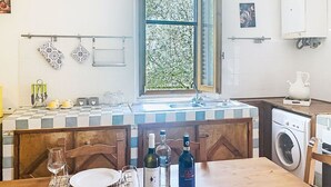 Una cocina con un salpicadero de baldosas a cuadros, una ventana con vistas a la vegetación, una lavadora y un comedor con una mesa lista para dos.
