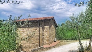 Un edificio de piedra con techo de tejas rojas, rodeado de olivos.