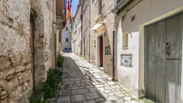 A narrow cobblestone alley with stone buildings, a wooden door, and laundry hanging outside.