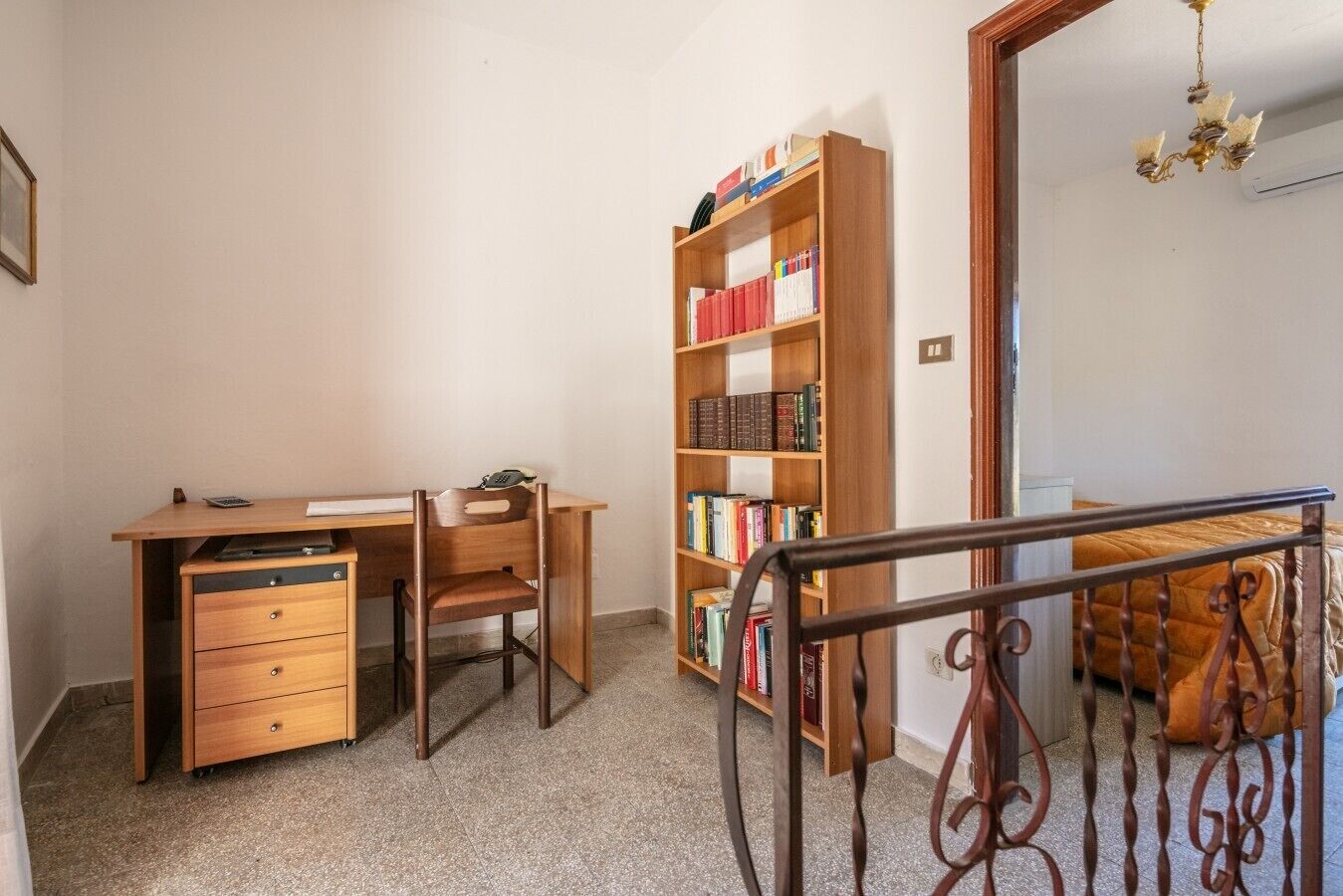 A study room with a desk, chair, bookshelf, and a staircase leading to a bedroom.