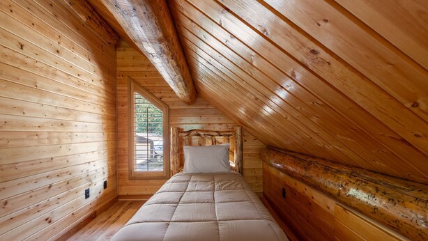 Interior de madera con una cama, una ventana y techo inclinado.