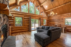 Ein Blockhaus-Interieur mit Kamin, einem Ecksofa und großen Fenstern, die einen Blick ins Freie bieten.
