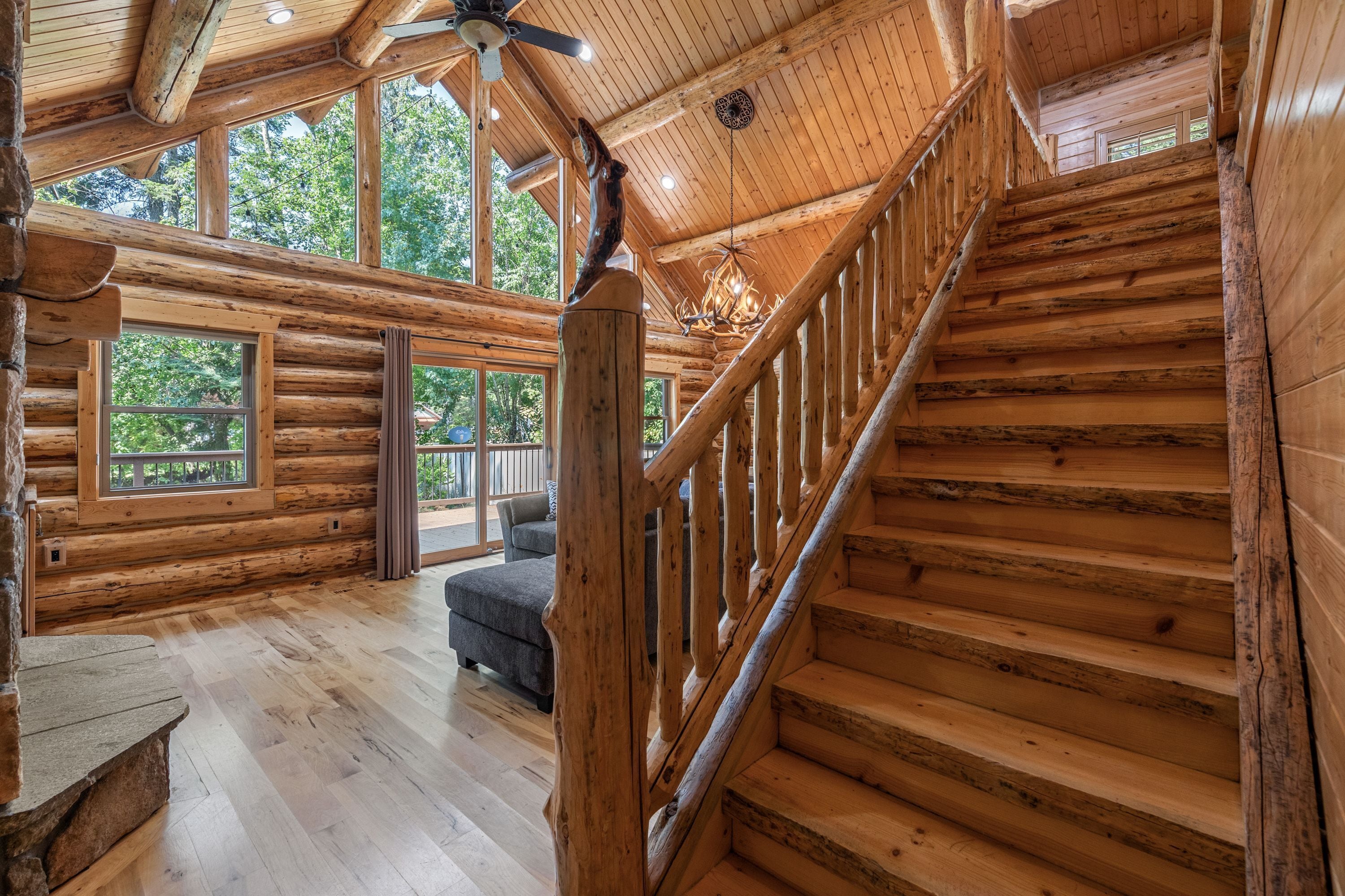 A log cabin interior with a staircase, large windows, and a chandelier.