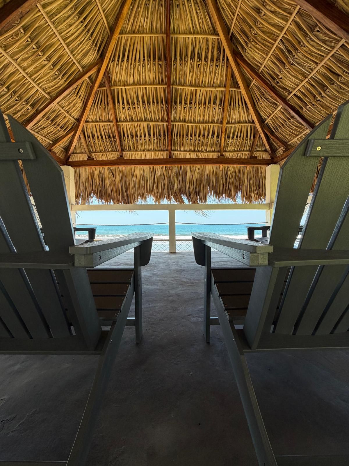 Una capanna sulla spiaggia con tetto di paglia, due panche di legno e vista sull'oceano.