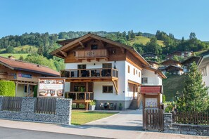 A two-story building with a balcony, a signboard, and a stone wall in front. - Appartement Neumayer (Viehhofen)
