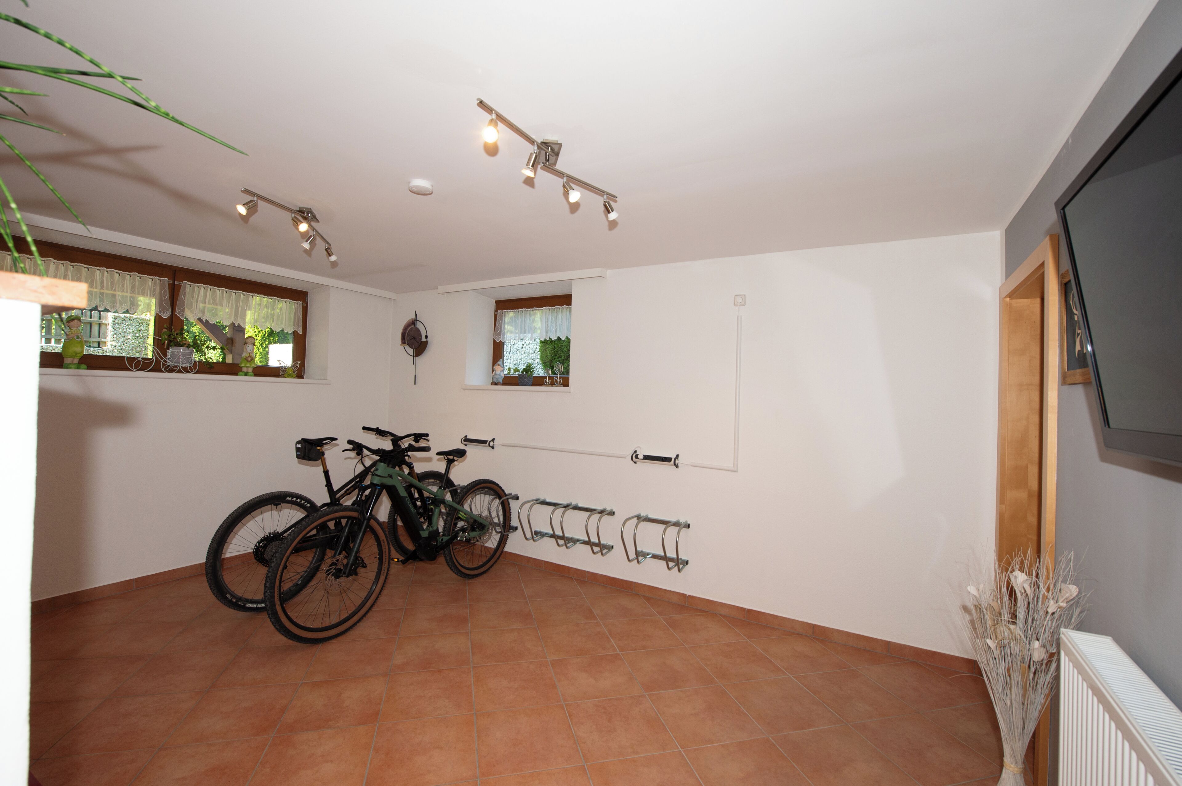 A spacious room with a tiled floor, two bicycles, a wall-mounted TV, and a window with a view of greenery.