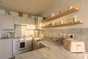 Eine Küche mit weißen Schränken, einer Marmorarbeitsplatte, einem Toaster und Holzregalen mit Küchenutensilien.