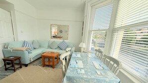 Ein Wohnzimmer mit einer Couch, einem Couchtisch, einem Esstisch mit Stühlen, einer Lampe und einem Fenster mit Jalousien.