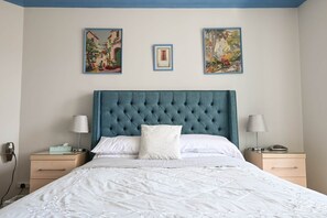 A bedroom with a tufted headboard, a bed with white linens, two bedside tables with lamps, and three framed artworks on the wall. - Bright 2‑Bed Apartment with Balcony, Sea Views & Parking in Central Swanage (Swanage)
