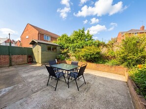 Eine Terrasse mit Tisch und Stühlen, eine kleine Gartenhütte und eine Backsteinmauer.