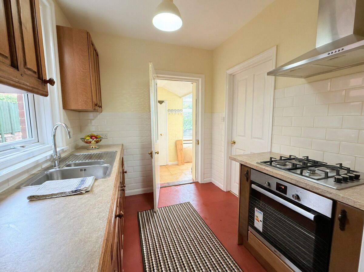 A kitchen with a gas stove, stainless steel sink, wooden cabinets, and a red floor mat.
