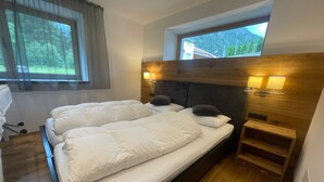 Una cama doble con cabecera de madera, lámparas de noche y una ventana con vistas a árboles.