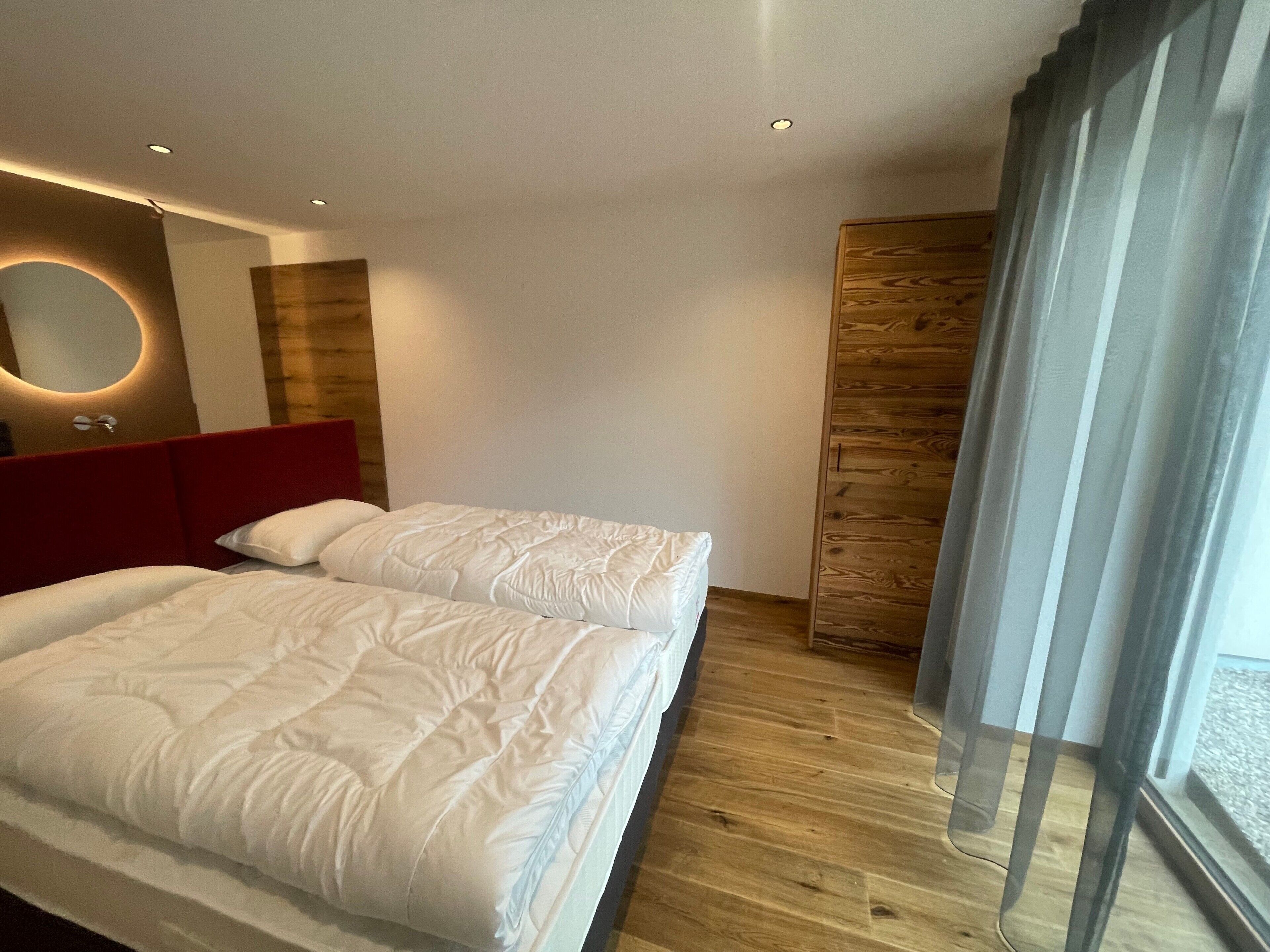 Une chambre d’hôtel moderne avec deux lits, un mur décoratif en bois, un miroir et une grande fenêtre.