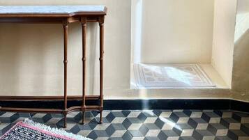 Een kamer met een houten tafel, een kapstok met hangers, een spiegel en een kamerbreed tapijt met een patroon.