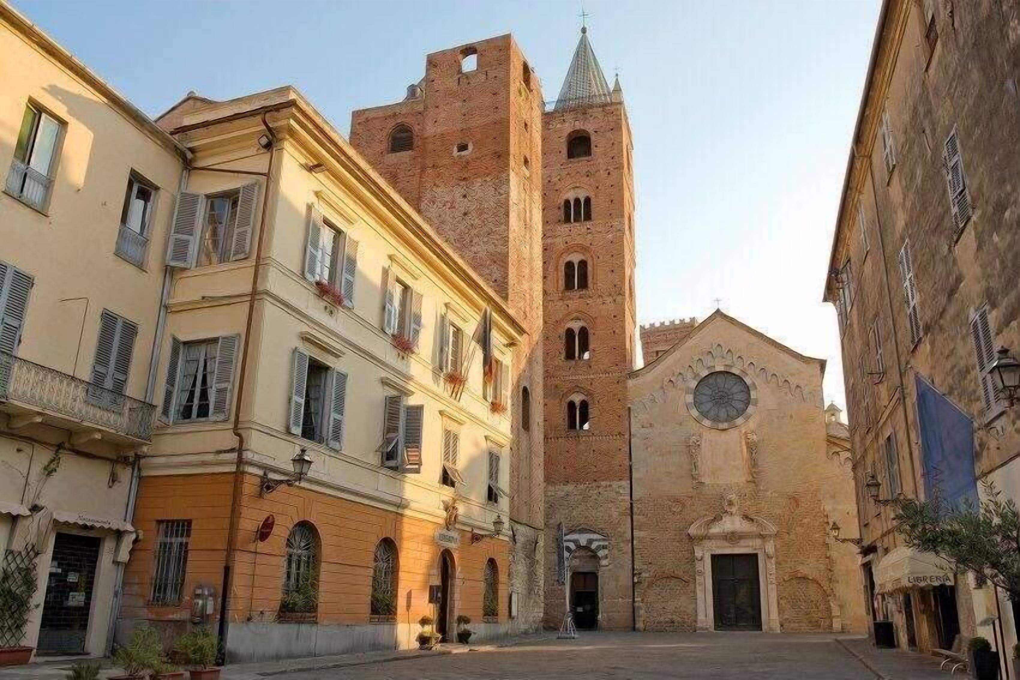 A narrow street with historic buildings, a prominent church with a clock tower, and a small square.