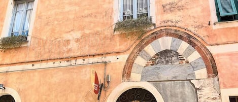 A building with a pink facade, multiple windows with shutters, and a door with a religious painting.