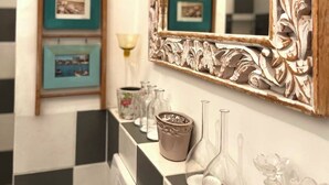 Une salle de bain avec un carrelage à motifs géométriques, un miroir doté d’un cadre en bois sculpté et des tableaux encadrés accrochés au mur.