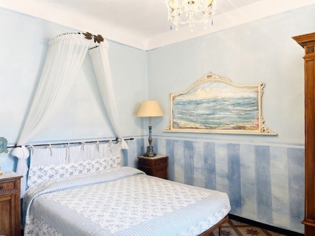A bedroom with a bed, a nightstand, a lamp, a painting, and a canopy.
