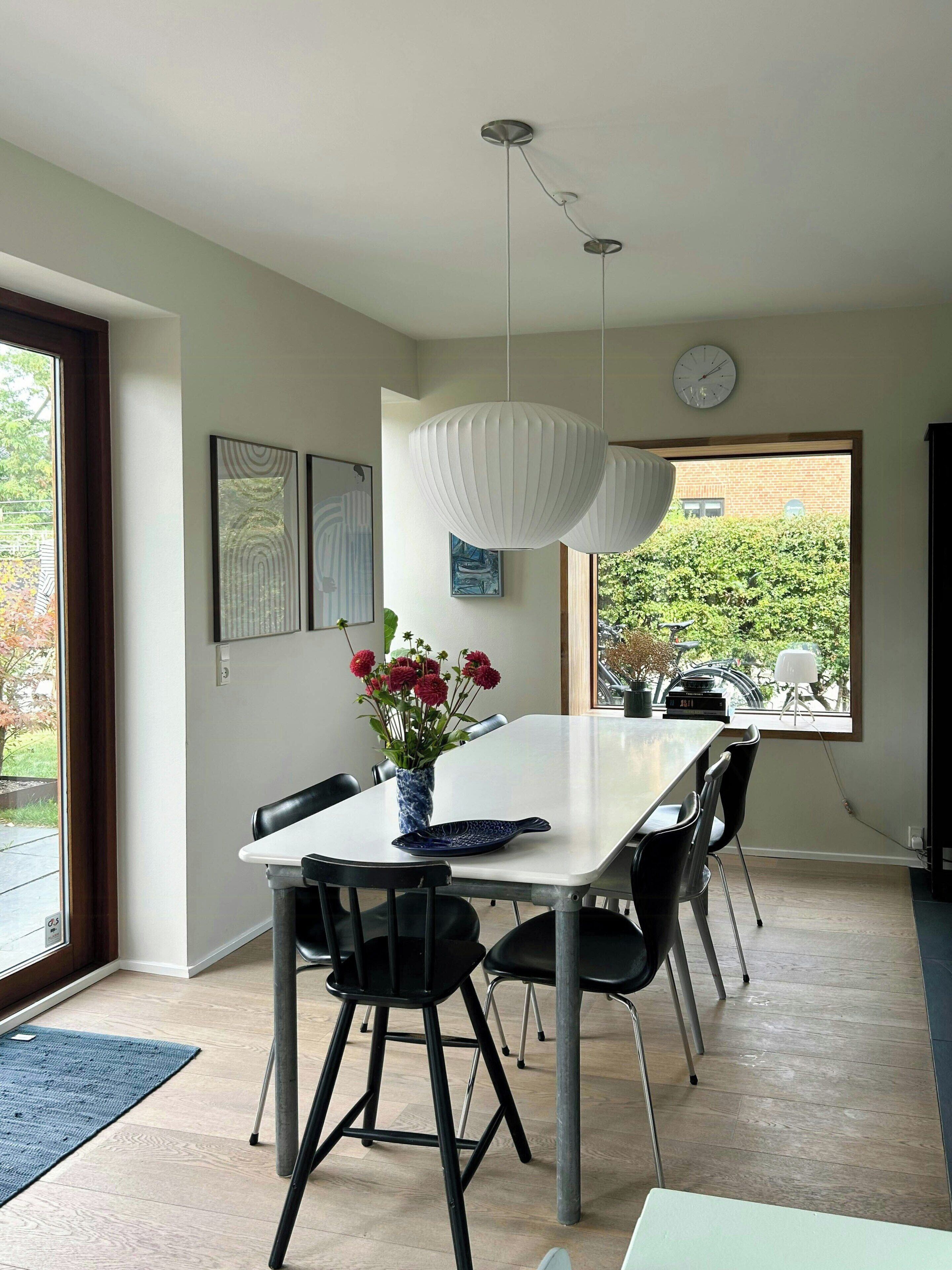 A modern dining area with a white table, black chairs, a vase with flowers, and pendant lights.