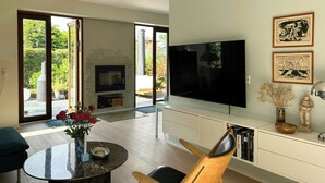 Ett modernt vardagsrum med en stor TV, en öppen spis och en matplats med ett runt bord och stolar.