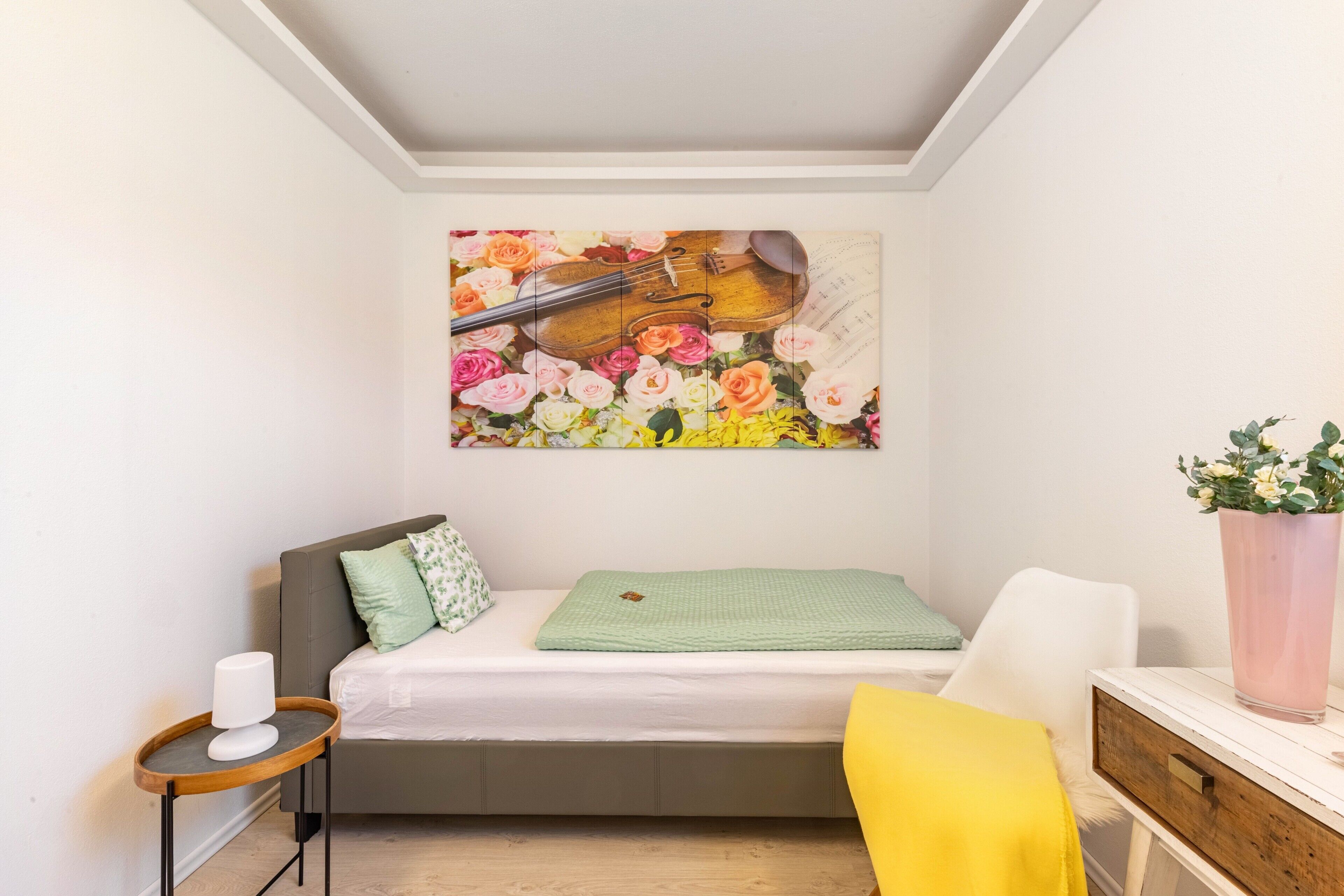 Ein Schlafzimmer mit Bett, Nachttisch, Stuhl, einem Gemälde und einer Zimmerpflanze.
