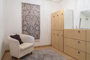 A room with a white armchair, a patterned curtain, a wooden wardrobe, and a mirror.