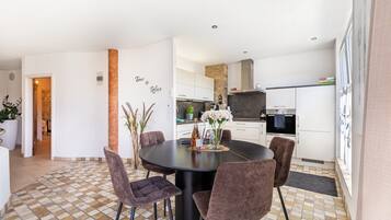 A modern kitchen with white cabinets, a central island, and a dining area with a round table and chairs.
