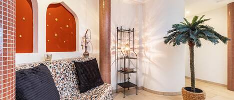 A modern interior with a patterned sofa, a tall column, a decorative lamp, and a potted palm tree.