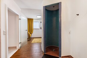 A hallway with a wooden floor, a glass door, a yellow curtain, and a blue-tiled shower area.