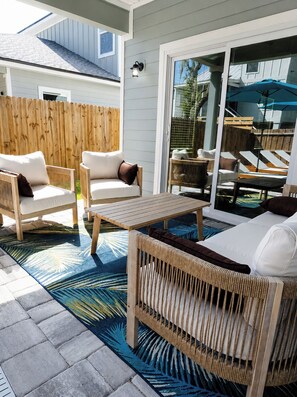 Eine Terrasse im Freien mit Korbmöbeln, einem Holztisch und einem gemusterten Teppich.