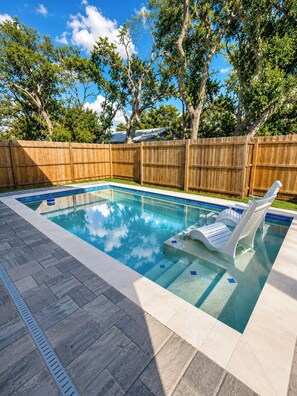 Ein rechteckiger Swimmingpool mit klarem, blauem Wasser, umgeben von einem Holenzaun und einer gepflasterten Terrasse.