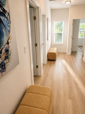 Un pasillo con piso de madera, un banco y una puerta que da a otra habitación.