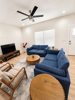 Una sala de estar moderna con un sofá modular, una mesa de centro de madera, un mueble para televisión y un ventilador de techo.
