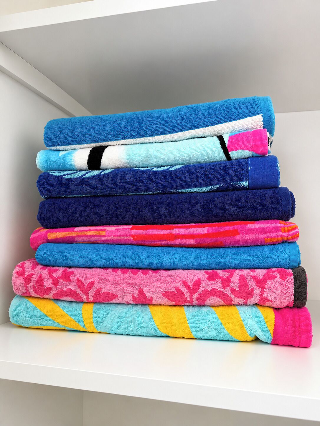 Uma pilha de toalhas dobradas em diversas cores e estampas sobre uma prateleira branca.