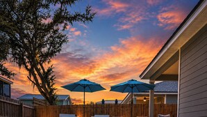 A swimming pool with lounge chairs and umbrellas, surrounded by a wooden fence and a house.