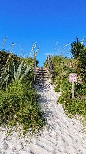 Ein sandiger Pfad, der zu einer Holztreppe mit einem Warnschild führt.