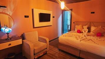 Une chambre avec un plafond en bois, un lit avec des oreillers et une couverture, une chaise, un bureau avec une lampe et un téléviseur fixé au mur.