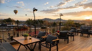 A terrace with outdoor seating, a table with a plant, and a view of the city and mountains. - NOVELA İN STONE HOUSE (Nevşehir)