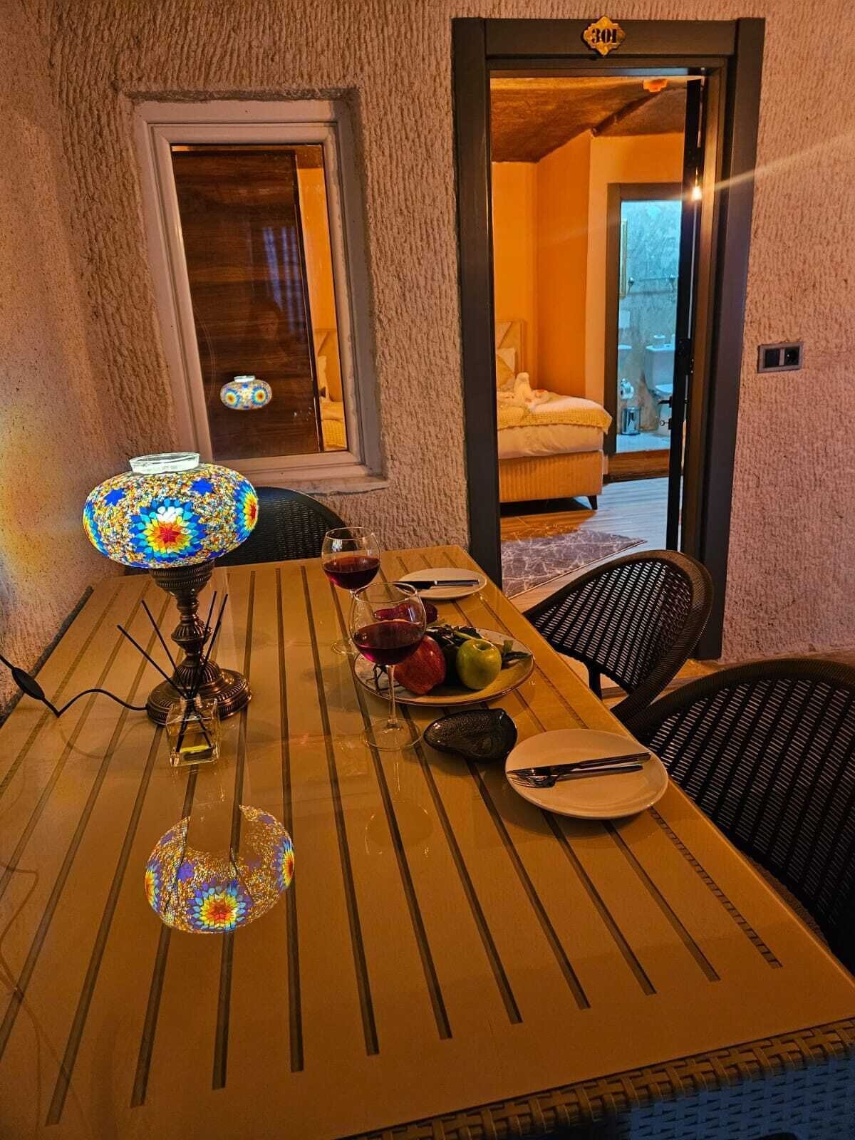 Una mesa de comedor con una lámpara decorativa, platos, cubiertos y un frutero.