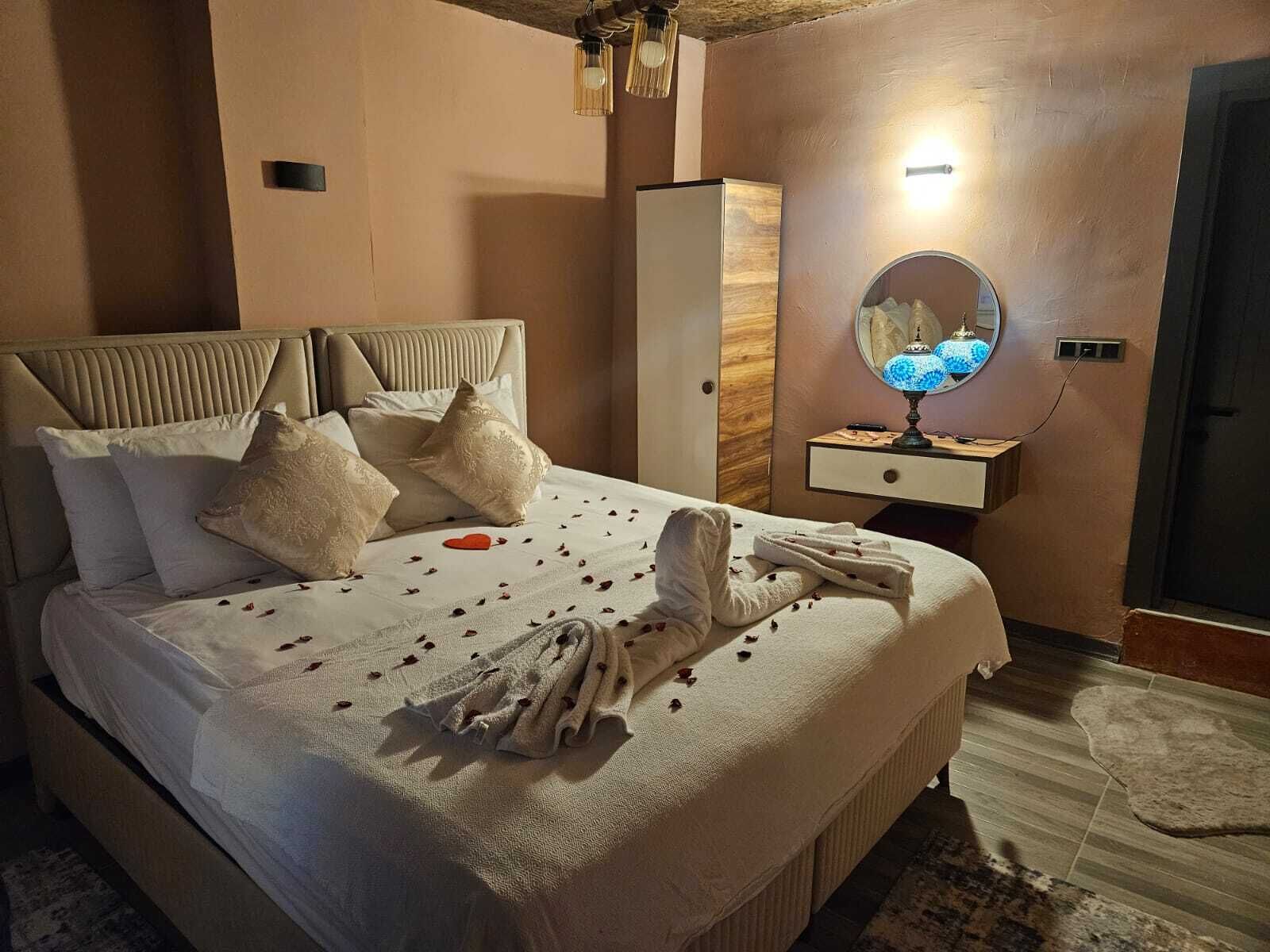 A neatly made bed with a heart-shaped decoration, a bedside lamp, and a mirror on a wooden nightstand.