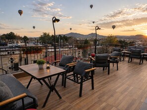 A rooftop terrace with outdoor seating, a view of the cityscape, and hot air balloons in the sky.
