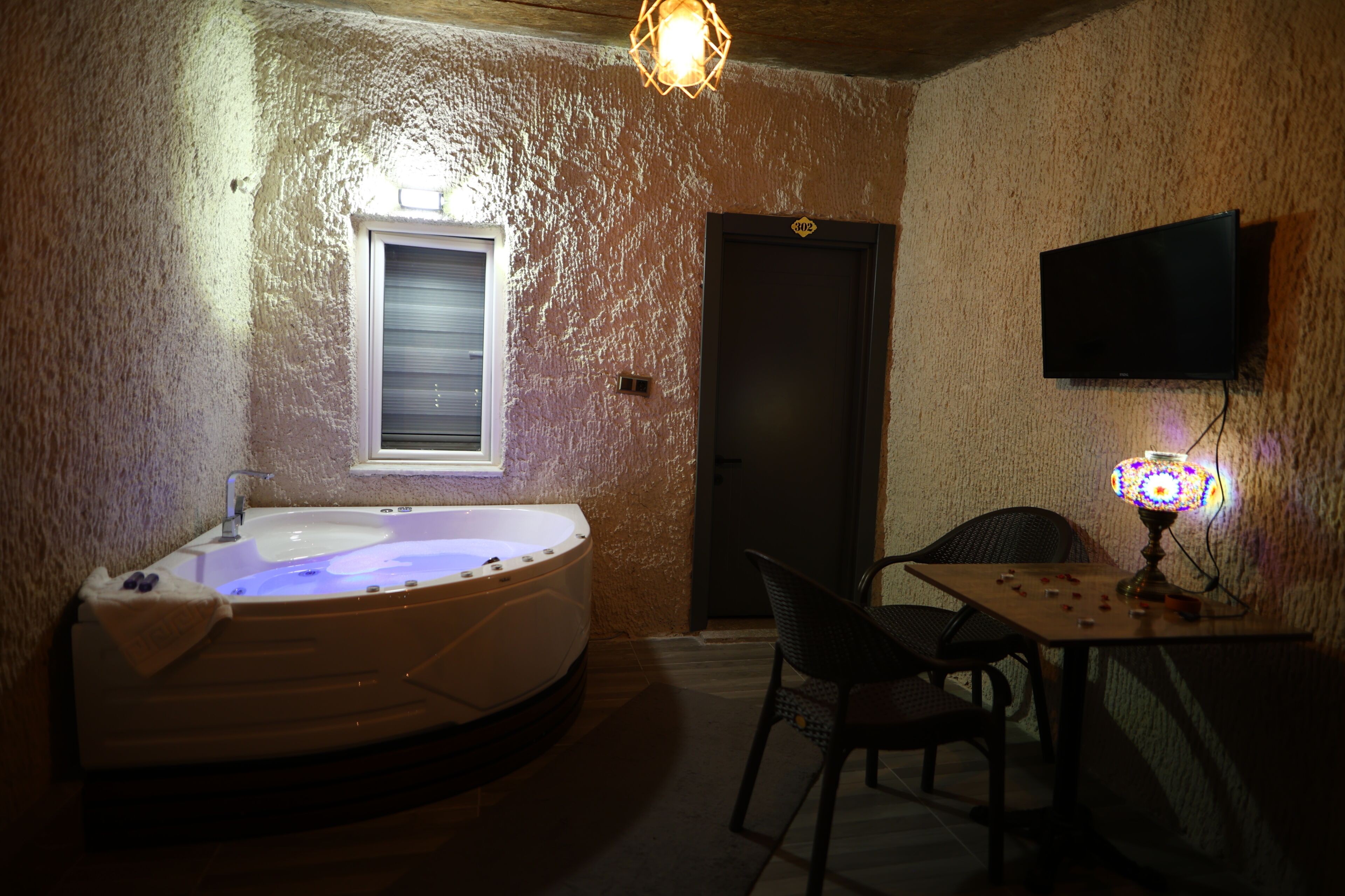 Una habitación con un jacuzzi, una mesa con objetos, una silla, un televisor y una puerta.