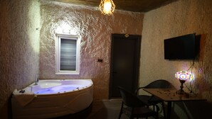 A room with a hot tub, a table with items, a chair, a television, and a door. - NOVELA İN STONE HOUSE (Nevşehir)