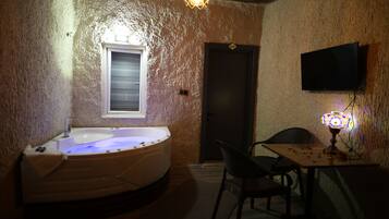 Una habitación con un jacuzzi, una mesa con objetos, una silla, un televisor y una puerta.