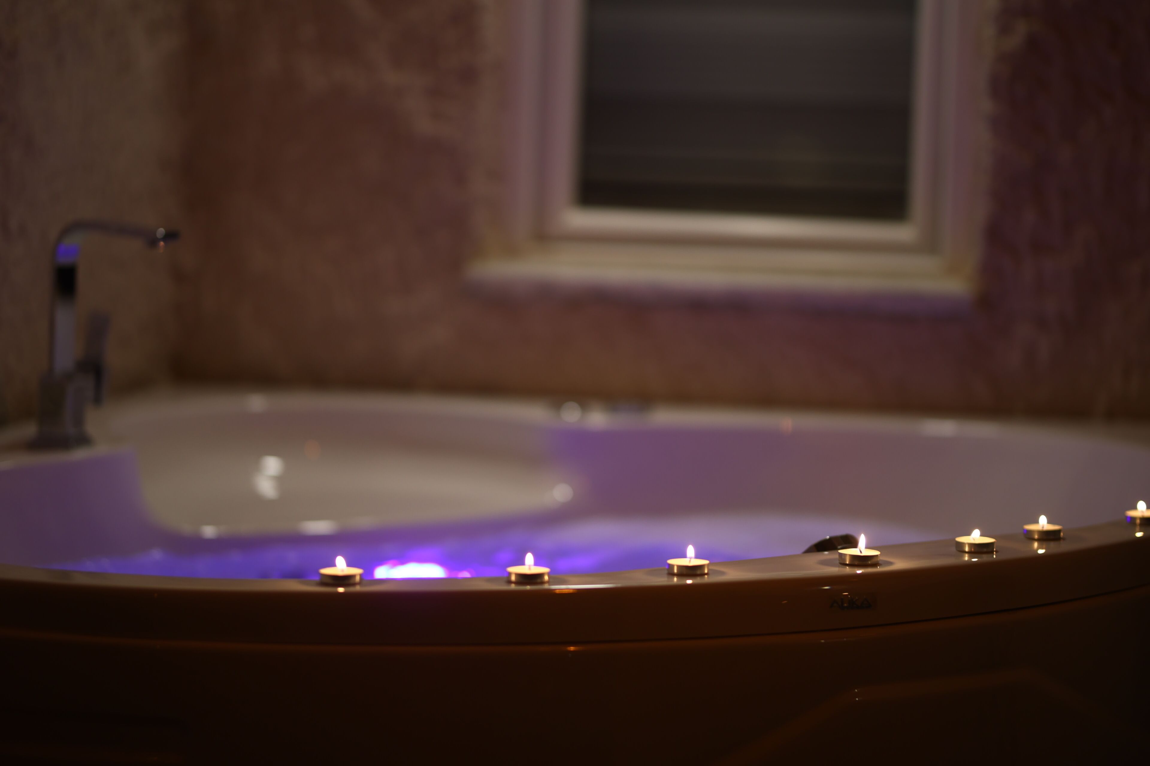 A bathtub with candles, a window, and a faucet.