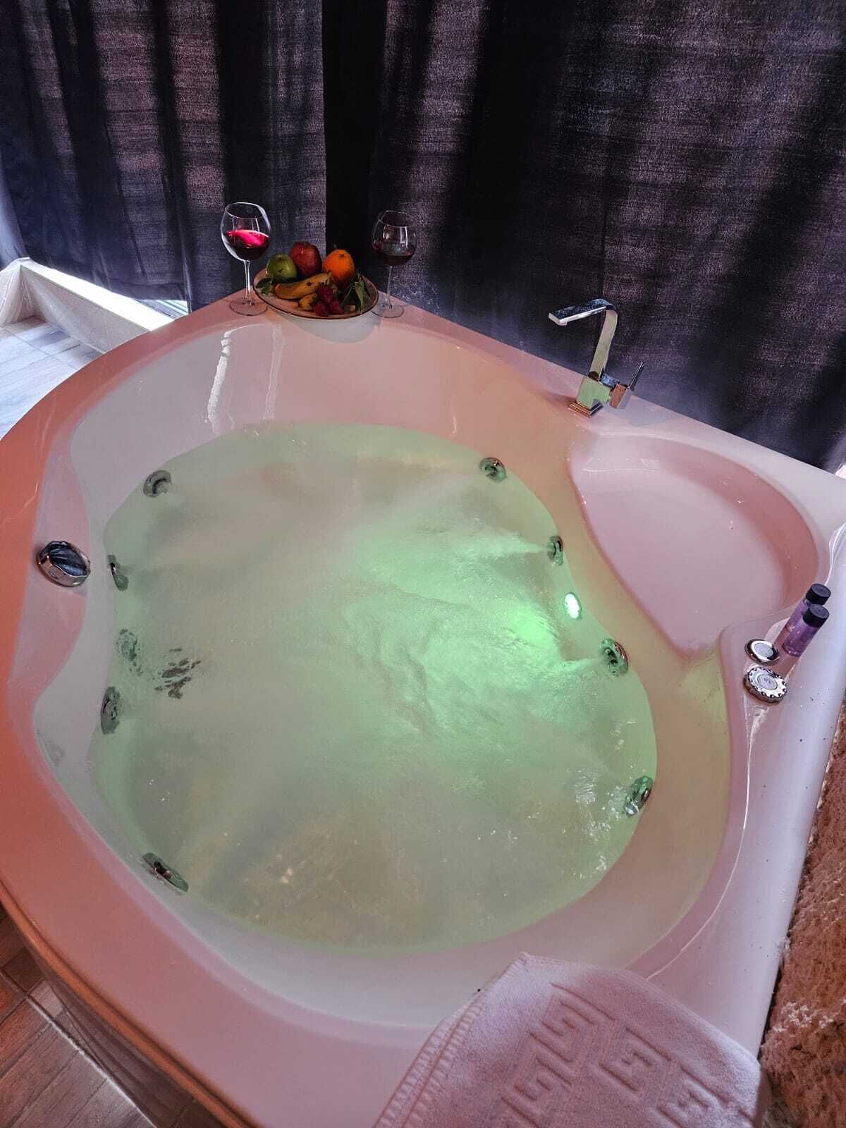 A bathtub with a greenish water tint, a towel, and a fruit bowl with apples and oranges.